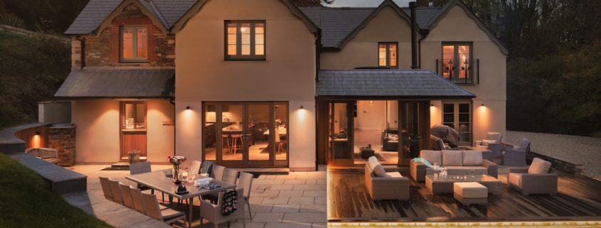 Rear view of the house at night with warm outdoor lighting and terraced seating areas